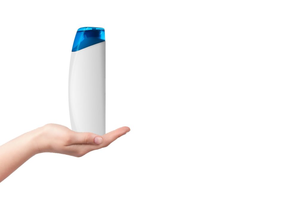 w dłoni butelka szamponu, białe tło